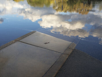 Sidewalk disappears into flood water, reflecting clouds.