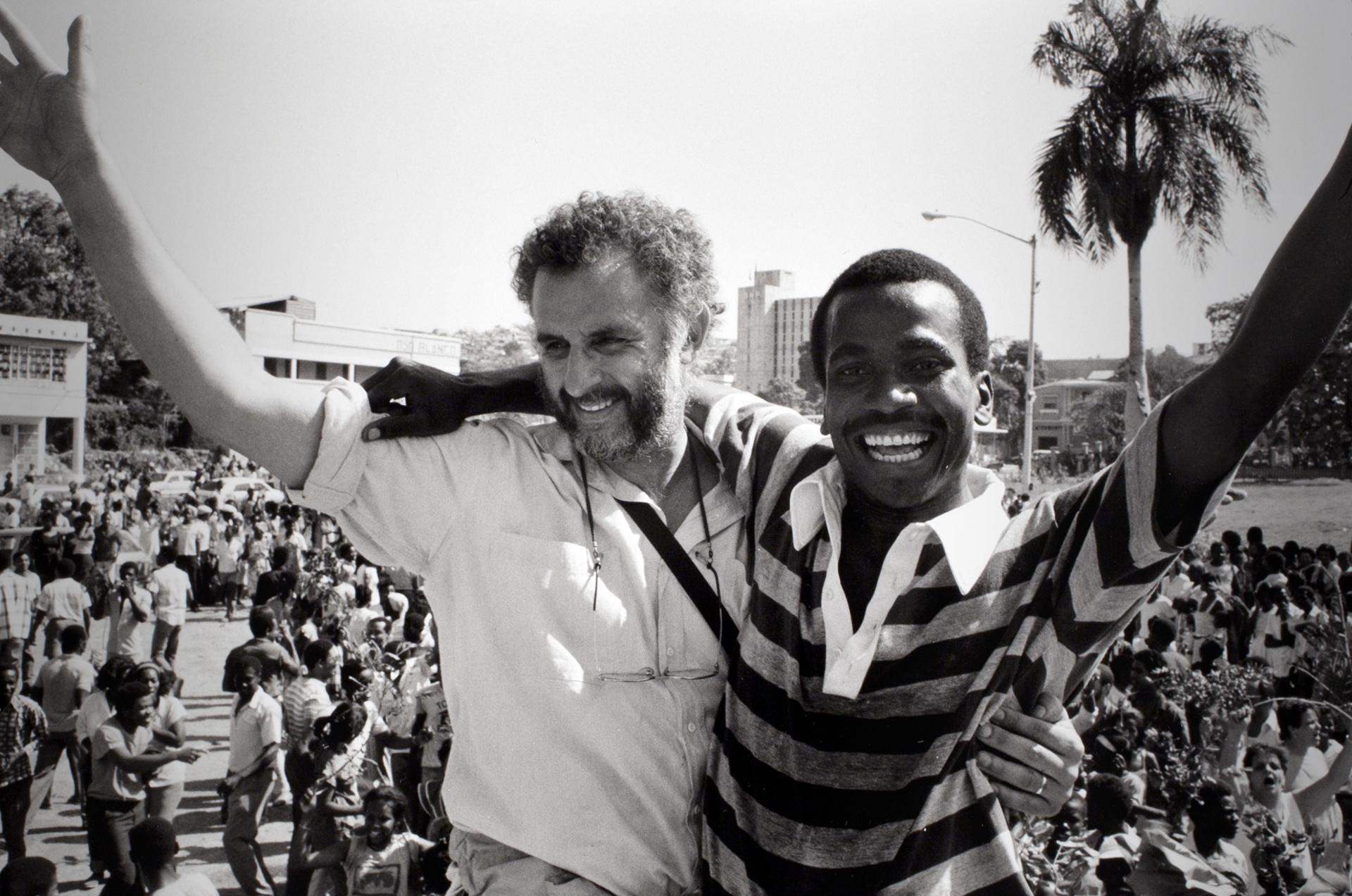 Danny Lyon and a man, each with one arm around the other person and one arm raised, stand above a crowd.