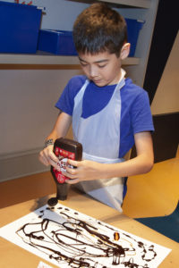 kid wearing an apron drawing with syrup