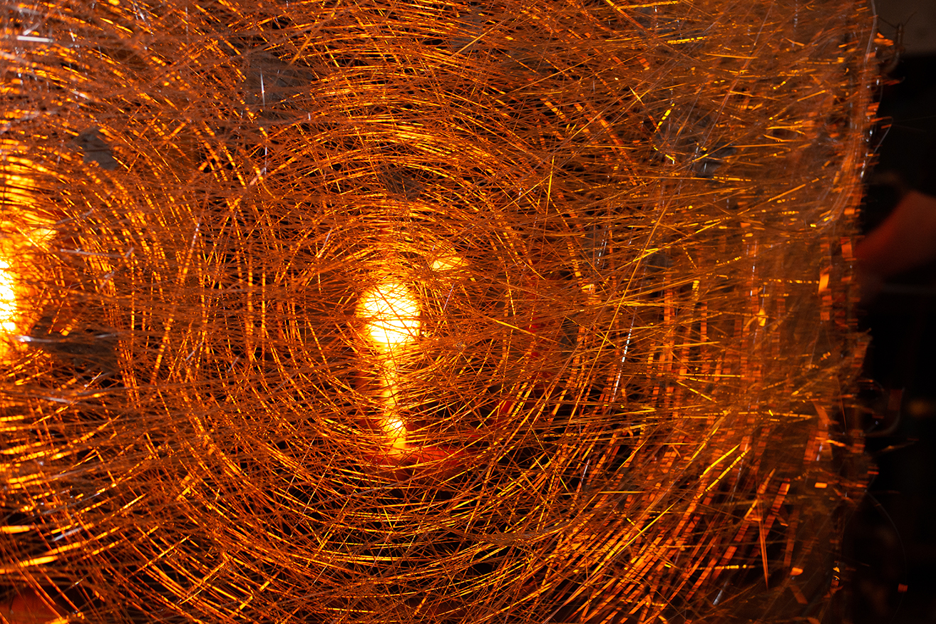 Glowing orange from a furnace behind spun glass.