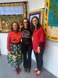 Artist Denise Walters poses in front of her quilt art with Higher Education and Outreach Coordinator, Julia Rogers, and Barry Curator of Glass, Carrie Needell.