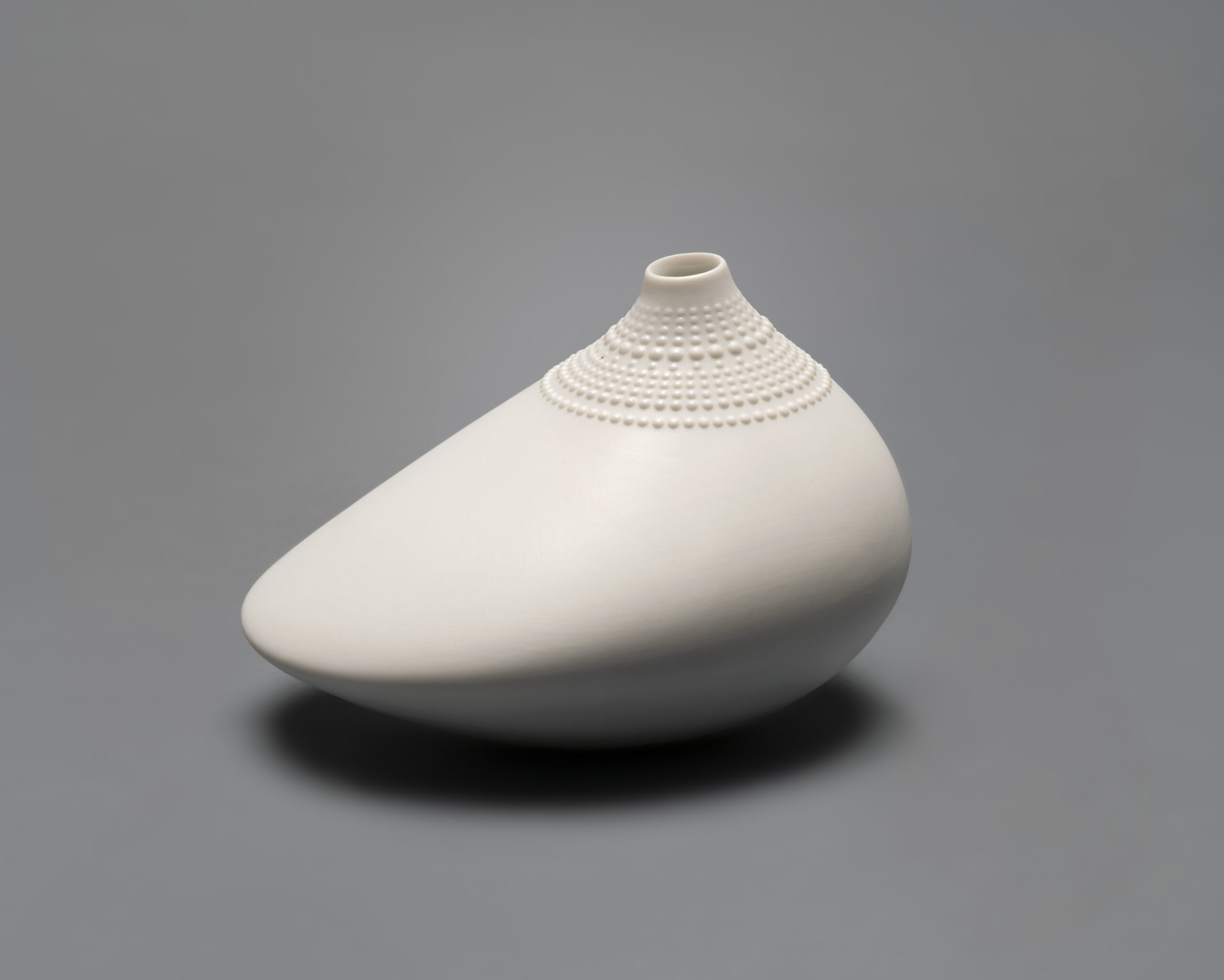 Asymmetrical, oblong porcelain vase with raised dots along the rim.