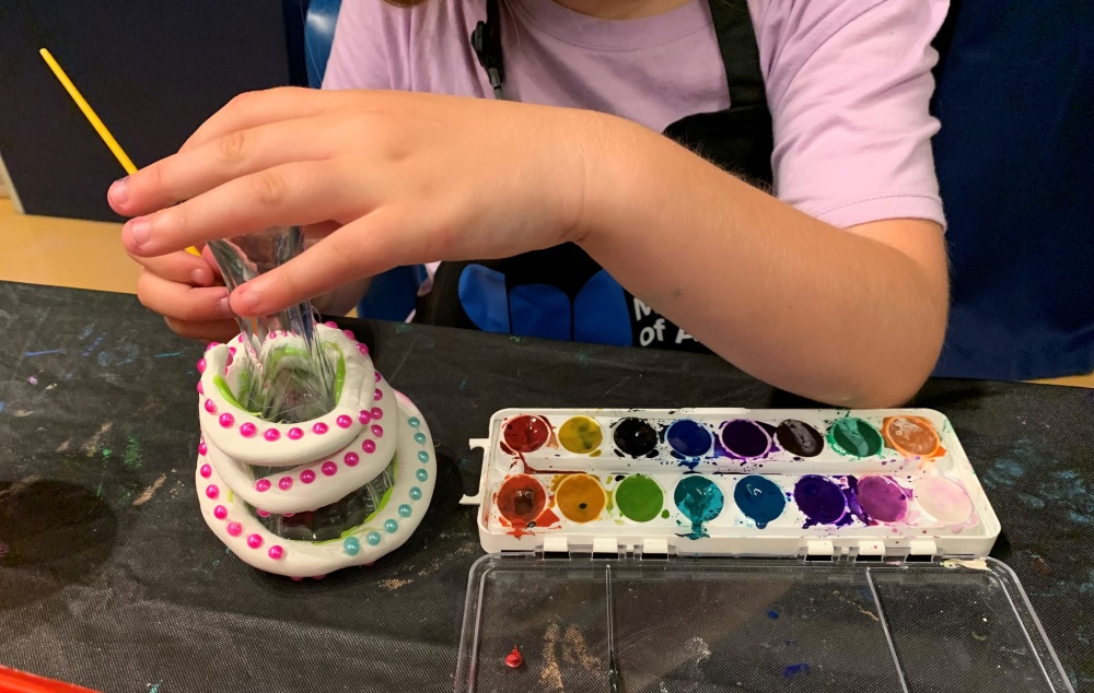 Child creating art with modeling clay, glass object, and water color paints