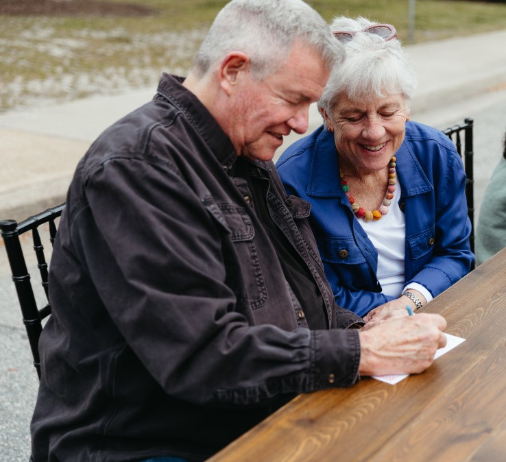 Older couple at table outside with pen and paper.