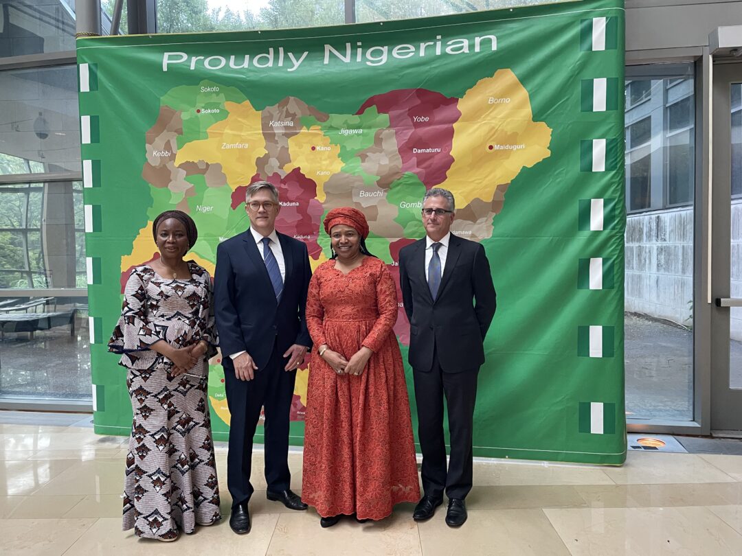 A group made up of people from the Nigerian embassy and the Chrysler Museum of Art stand in front of a banner that reads "Proudly Nigerian."