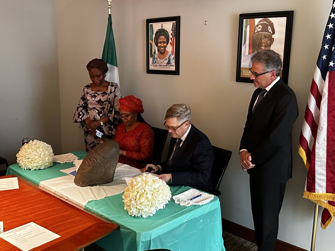 Representatives from the Chrysler Museum at the Embassy of the Federal Republic of Nigeria in Washington D.C. on Friday, June 23, for a Repatriation Ceremony. The two groups sign a document with the Bakor monolith displayed in front.