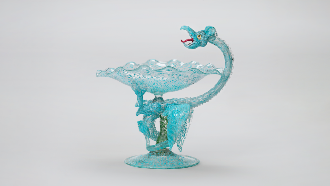 A dragon twists around the stem of a glass goblet forming the handle.