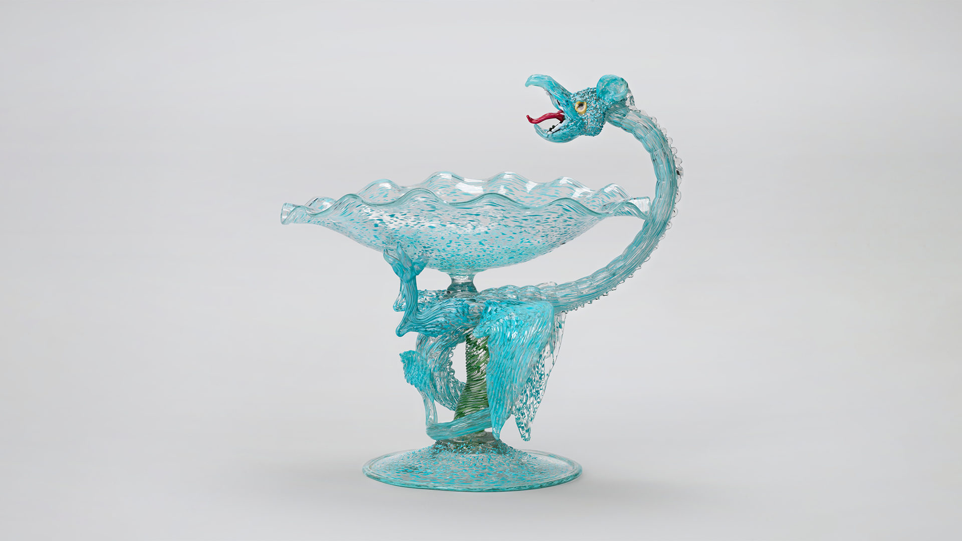 A dragon twists around the stem of a glass goblet forming the handle.