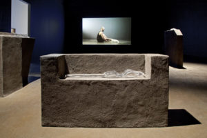 Installation image with plith and crystal ballet foot stretcher. Video playing in background.