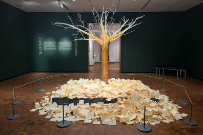 Jaime Guerrero's glass tree stands in the center of a gallery, with thousands of notes left by visitors scattered along the base of the tree.