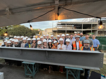 The Chrysler team, board members, stakeholders, and the construction and design teams stand behind a beam covered in their signatures.
