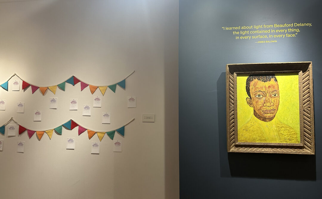 Portrait of James Baldwin bathed in a golden light hangs next to birthday messages left by visitors.