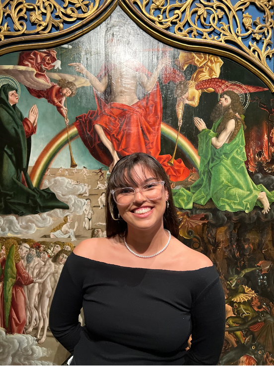 2023 Summer Intern Isabel Grewatz stands smiling in front of her favorite painting in the collection, "The Last Judgment" by Marx Reichlich.