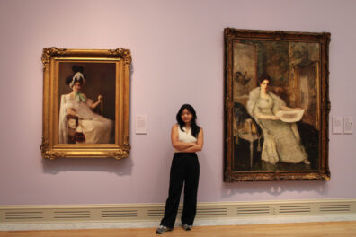 Sophia Kim stands between a painting by artist Susan Watkins and a portrait of the artist.