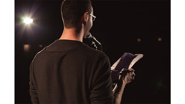 man with his back to us on a stage reading from a paper
