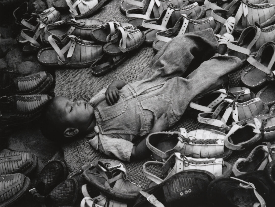 Photograph of a sleeping child surrounded by shoes and sandals.